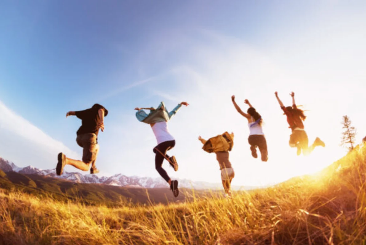 Group of five happy friends runs and jumps against mountains at sunset time. Travel or expeditions concept